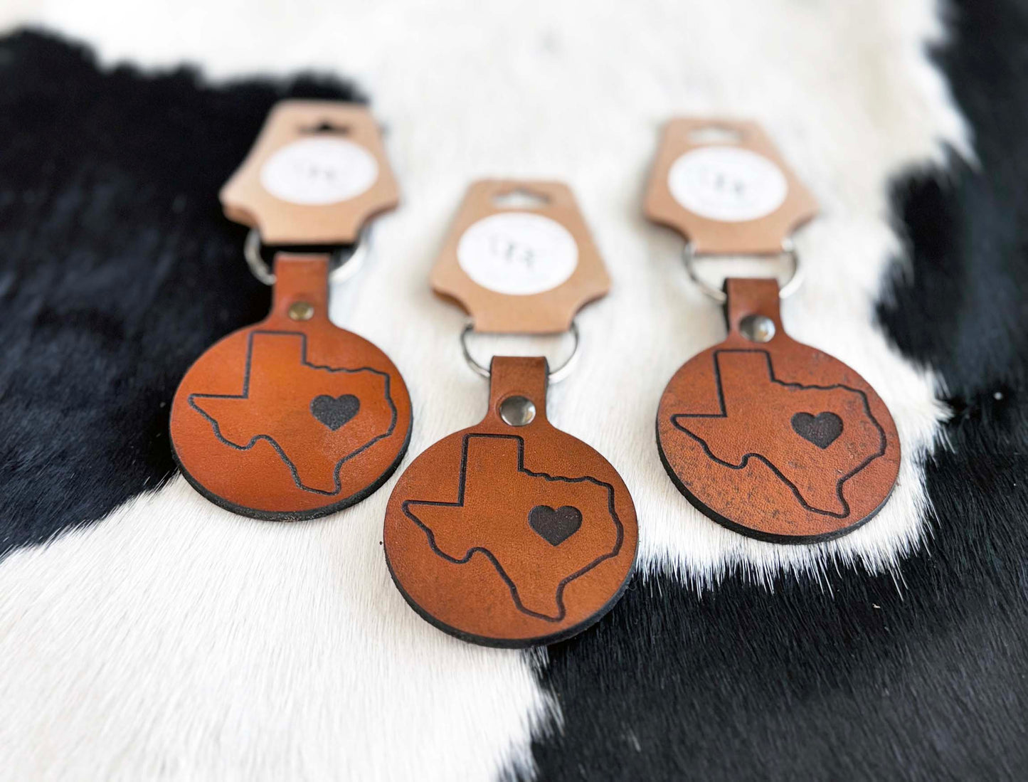 A series of leather keychains with a Texas shape and a heart design, displayed on a furry surface.