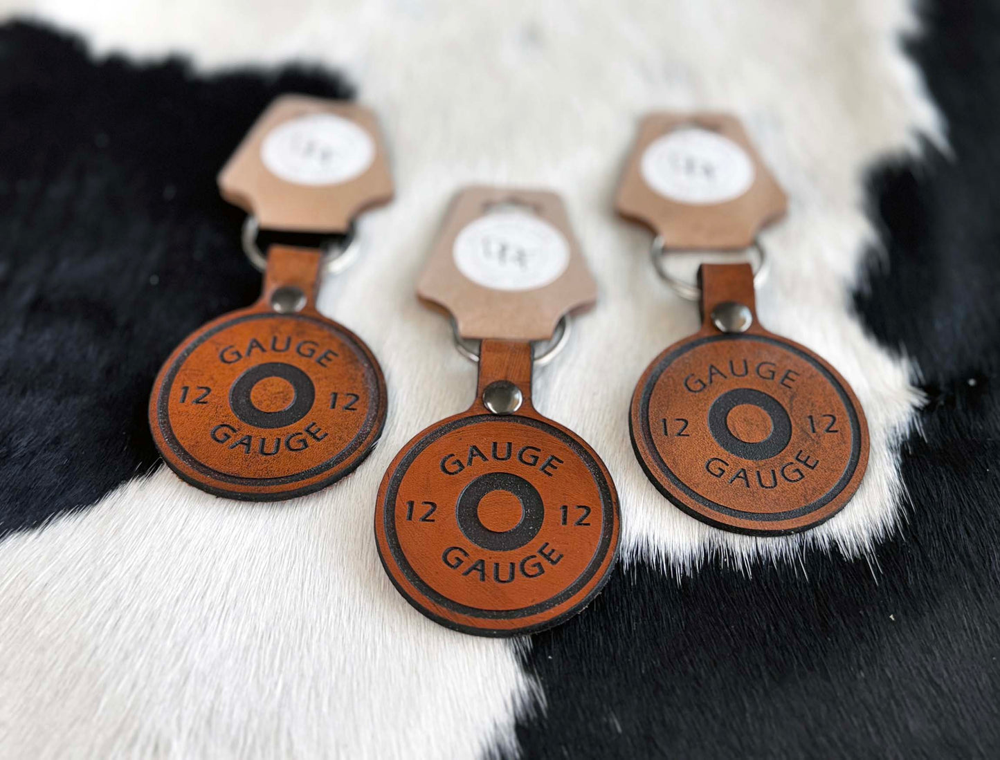 Three leather keychains shaped like shotgun shells with the numbers 12 and the word 'GAUGE' embossed on them, displayed on a furry surface.