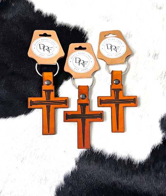 Three leather keychains shaped like crosses with brown and white colors, displayed on a furry surface.