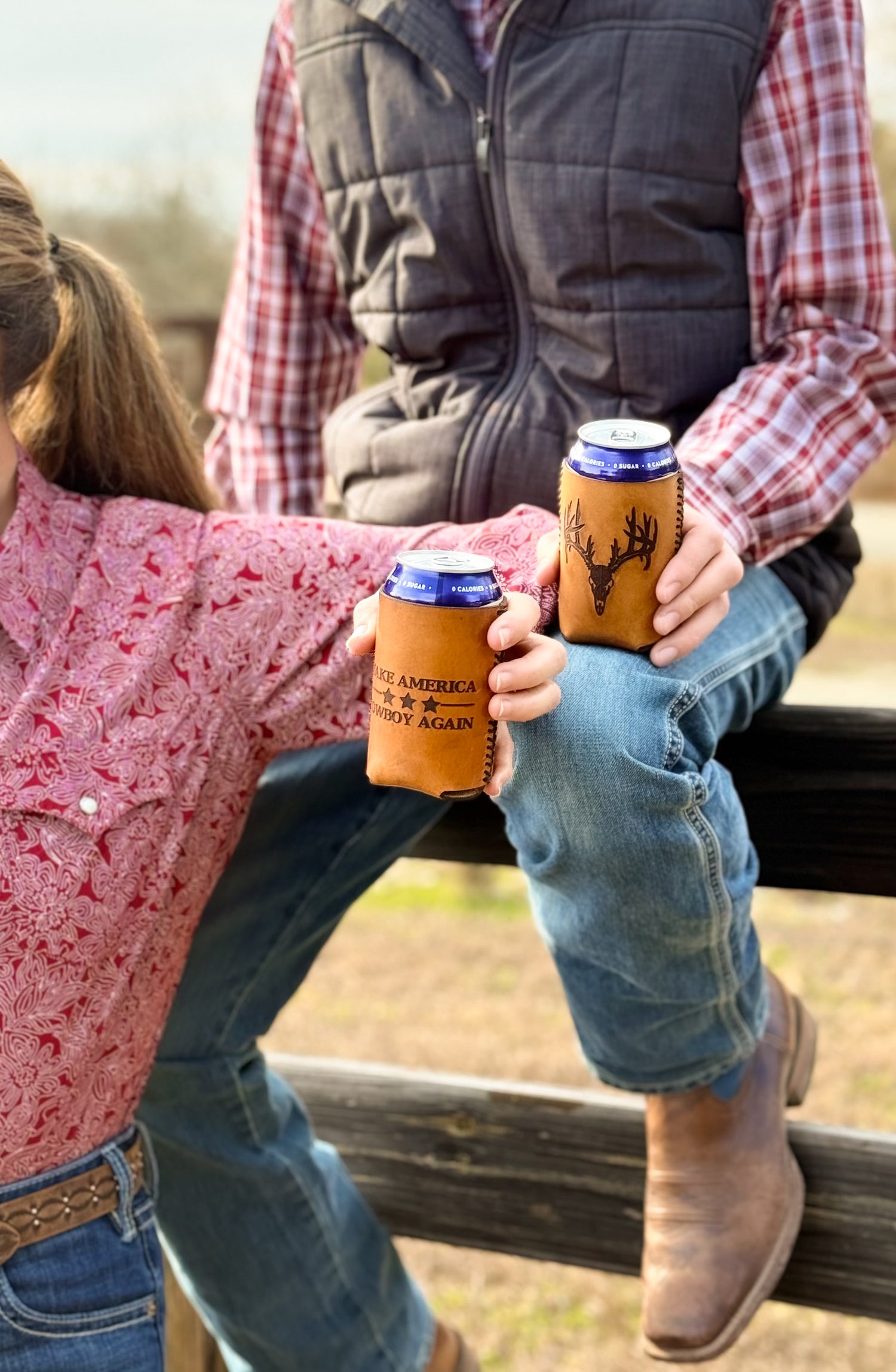 Two people sitting on a fence holding branded can coolers.