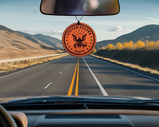 Navy emblem air freshener hanging from a car's rearview mirror with a scenic road view.
